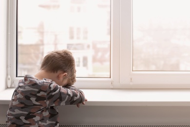 Lonely little boy near window indoors. Child autism