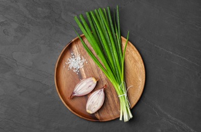 Bunch of fresh green onion and halved bulb on black table, top view