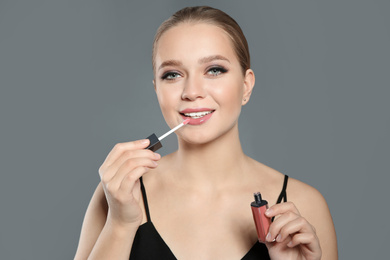 Beautiful woman applying lip gloss on light grey background. Stylish makeup