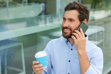 Photo of Handsome man with cup of coffee talking on phone outdoors