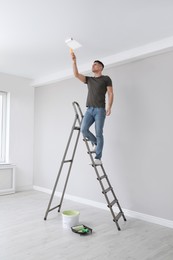 Photo of Man painting ceiling with roller on step ladder in room