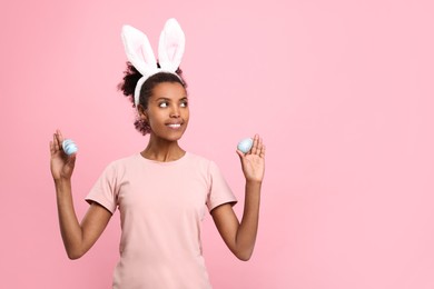 Photo of Happy African American woman in bunny ears headband holding Easter eggs on pink background, space for text