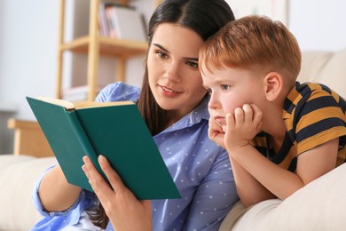 Mother reading book with her son in living room at home