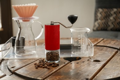 Manual coffee grinder with beans, glass jug and wave dripper on wooden table in cafe