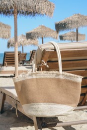 Straw bag on wooden sunbed near sea. Beach accessory