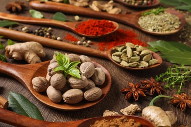 Different herbs and spices with spoons on wooden table, closeup