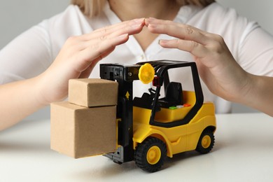 Photo of Woman covering toy forklift at white table, closeup. Logistics and wholesale concept