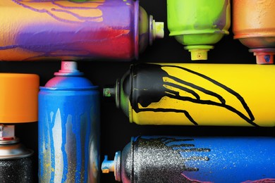 Used cans of spray paints on black background, flat lay. Graffiti supplies