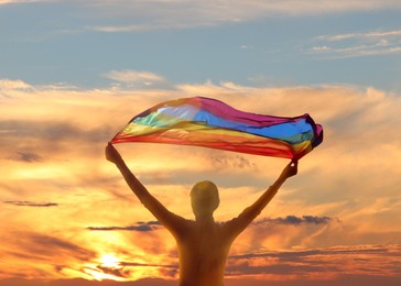 Woman with bright LGBT flag against sky at sunset