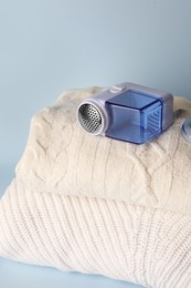 Photo of Modern fabric shaver and knitted clothes on light blue background