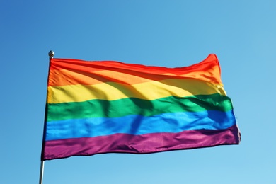 Rainbow LGBT flag fluttering on blue sky background. Gay rights movement