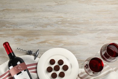 Glasses and bottle of red wine with chocolate candies on white wooden table, flat lay. Space for text