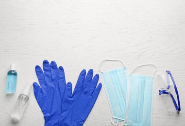 Flat lay composition with medical gloves, masks and hand sanitizers on white wooden background. Space for text