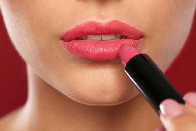 Young woman applying lipstick on color background, closeup