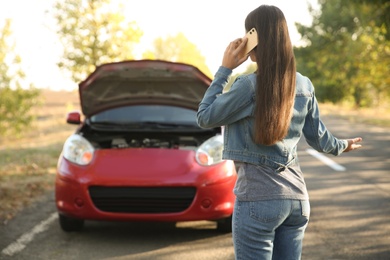 Young woman talking on phone near broken car outdoors, back view