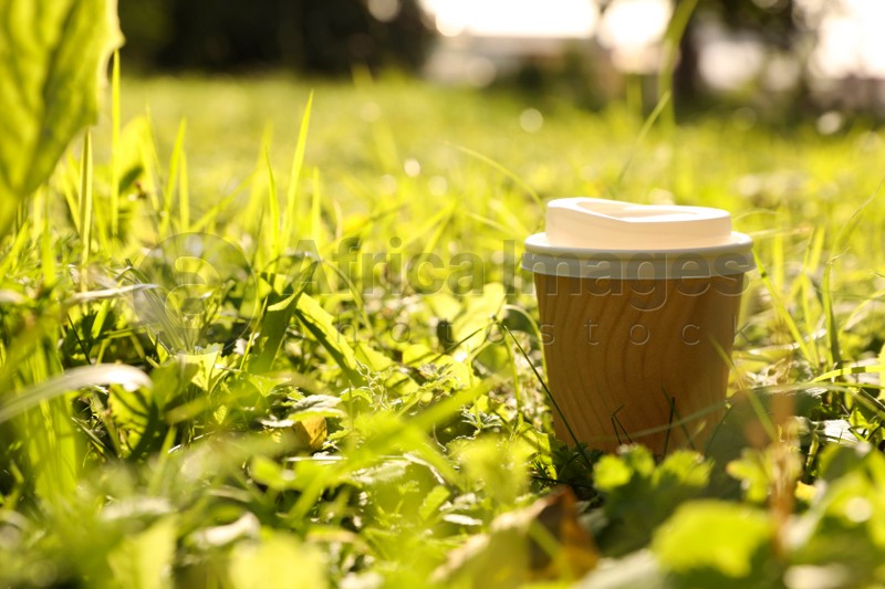 Paper cup on green grass outdoors, space for text. Coffee to go