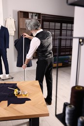 Professional tailor with measuring tape working in atelier
