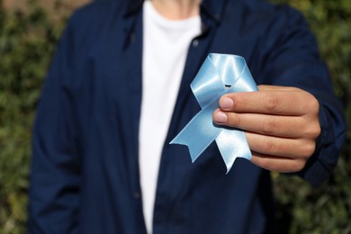Man holding light blue ribbon outdoors, closeup. World Diabetes Day