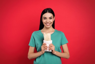 Photo of Happy young woman with delicious shawarma on red background
