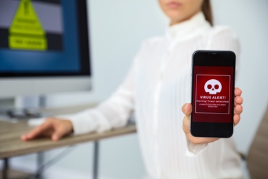 Woman holding smartphone with warning about virus attack in office, closeup. Space for text