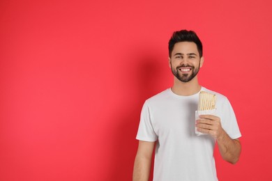 Photo of Happy young man holding tasty shawarma on red background. Space for text