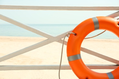 Orange life buoy near wooden railing on beach, closeup.  Emergency rescue equipment