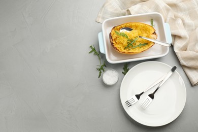 Half of cooked spaghetti squash with arugula in baking dish, plate and cutlery on grey table, flat lay. Space for text