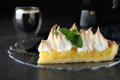 Piece of delicious lemon meringue pie with mint served on black table, closeup
