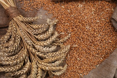 Photo of Sack with wheat grains and spikelets on wooden table, top view