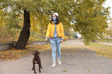 Woman in protective mask with German Shorthaired Pointer in park. Walking dog during COVID-19 pandemic