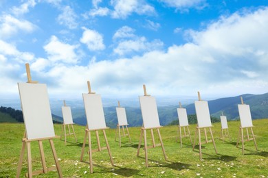 Wooden easels with blank canvases in mountains on sunny day 