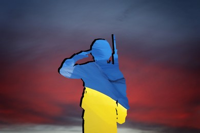 Silhouette of soldier in color of Ukrainian flag with assault rifle against sky at sunset