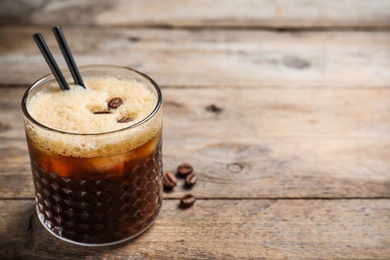 Glass of tasty refreshing cocktail with coffee beans on wooden table. Space for text