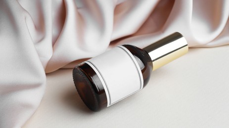 Photo of Bottle of luxurious perfume and beige silk fabric on light background, closeup