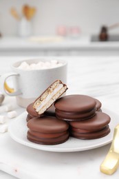 Saucer with delicious choco pies and cup of drink on white table in kitchen