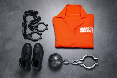 Prisoner ball with chain, jail clothes and boots on grey table, flat lay