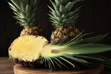 Photo of Whole and cut pineapples on wooden board, closeup