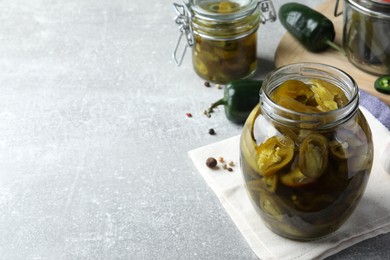 Photo of Glass jar with slices of pickled green jalapeno peppers on light grey table, space for text