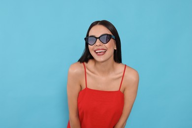 Attractive happy woman in fashionable sunglasses against light blue background