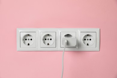 Charger adapter plugged into power sockets on pink wall. Electrical supply