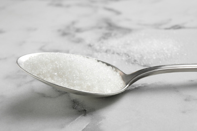 Photo of Spoon of white sugar on marble table, closeup