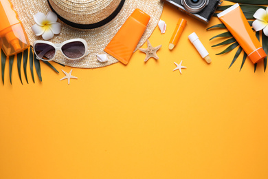 Sun protection products and beach accessories on orange background, flat lay. Space for text
