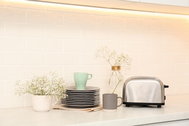 Modern toaster, crockery and flowers on counter in kitchen