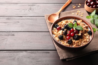 Photo of Bowl of muesli served with berries and milk on wooden table, space for text
