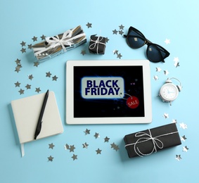 Flat lay composition with tablet, gifts and accessories on light blue background. Black Friday sale
