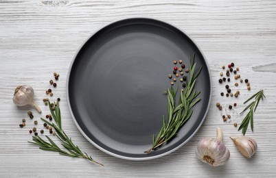 New dark plate with rosemary, garlic and peppercorns on light wooden table, flat lay