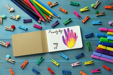 Notebook with text Family Day May 15 and paper cutout surrounded by colorful stationery on light blue wooden table, flat lay
