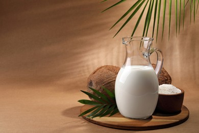 Photo of Glass jug of delicious vegan milk, coconuts, flakes and palm leaf on brown background. Space for text