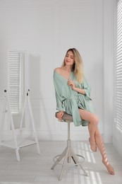 Pretty young woman in beautiful silk robe sitting on stool at home