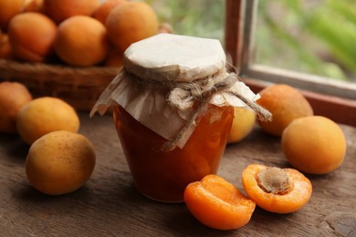 Jar of delicious jam and fresh ripe apricots on wooden table indoors. Fruit preserve